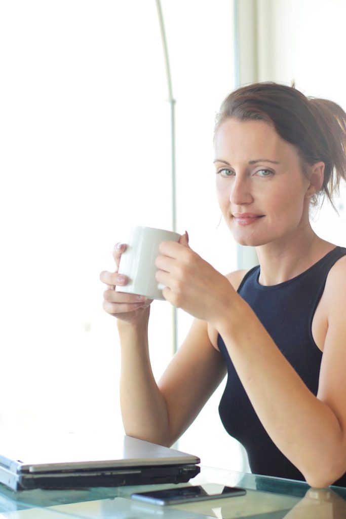 Young woman sitting at her desk, holding a coffee cup and smiling. Ideal for workplace and lifestyle themes.